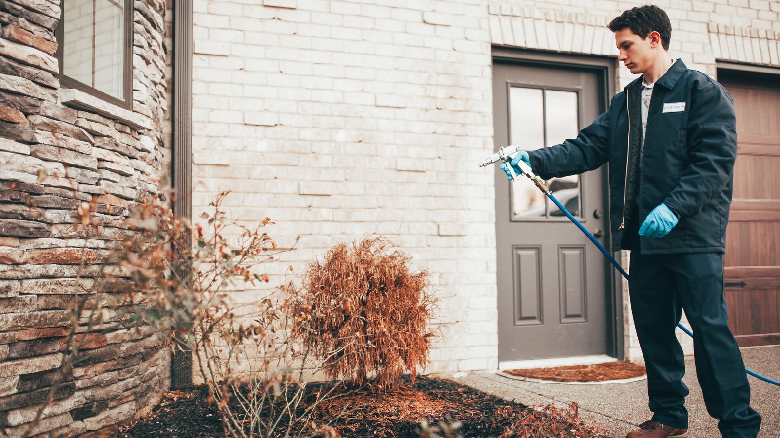 An Urbanex technician treating the foundation beds of a brick home