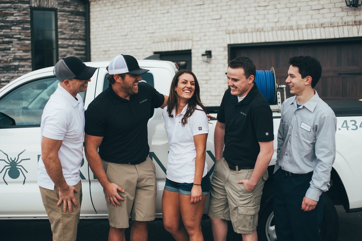 Urbanex technicians laughing together beside a service truck at the start of the day