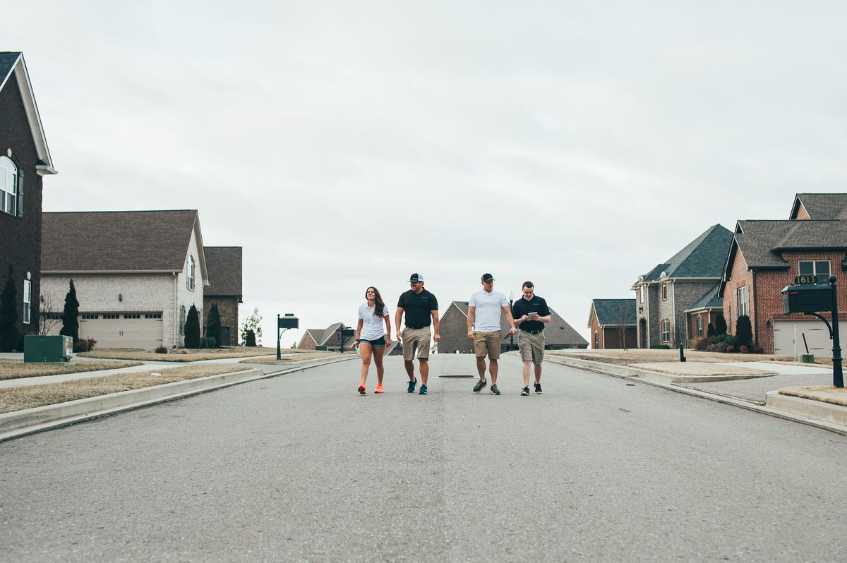 Urbanex technicians walking a wide residential subdivision street lined with brick homes