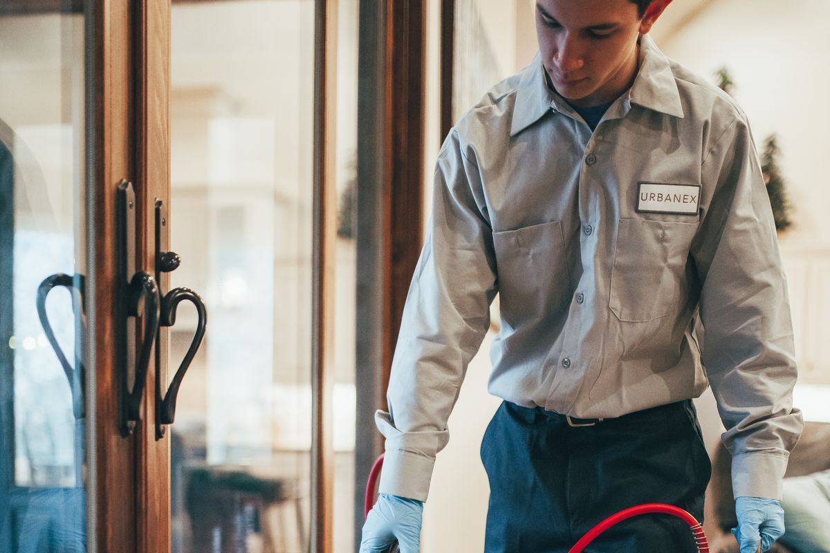 An Urbanex technician treating baseboards inside a home beside the patio doors
