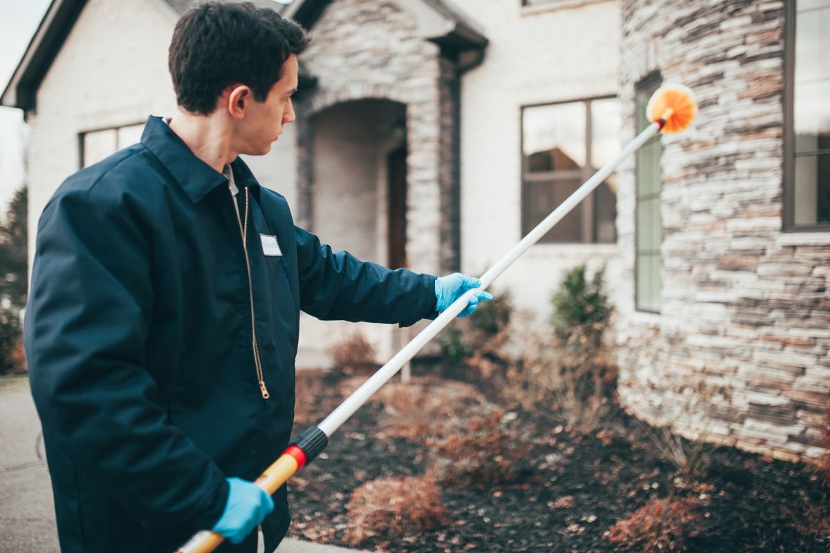 An Urbanex technician removing webs from a home's eaves and windows with an extension pole