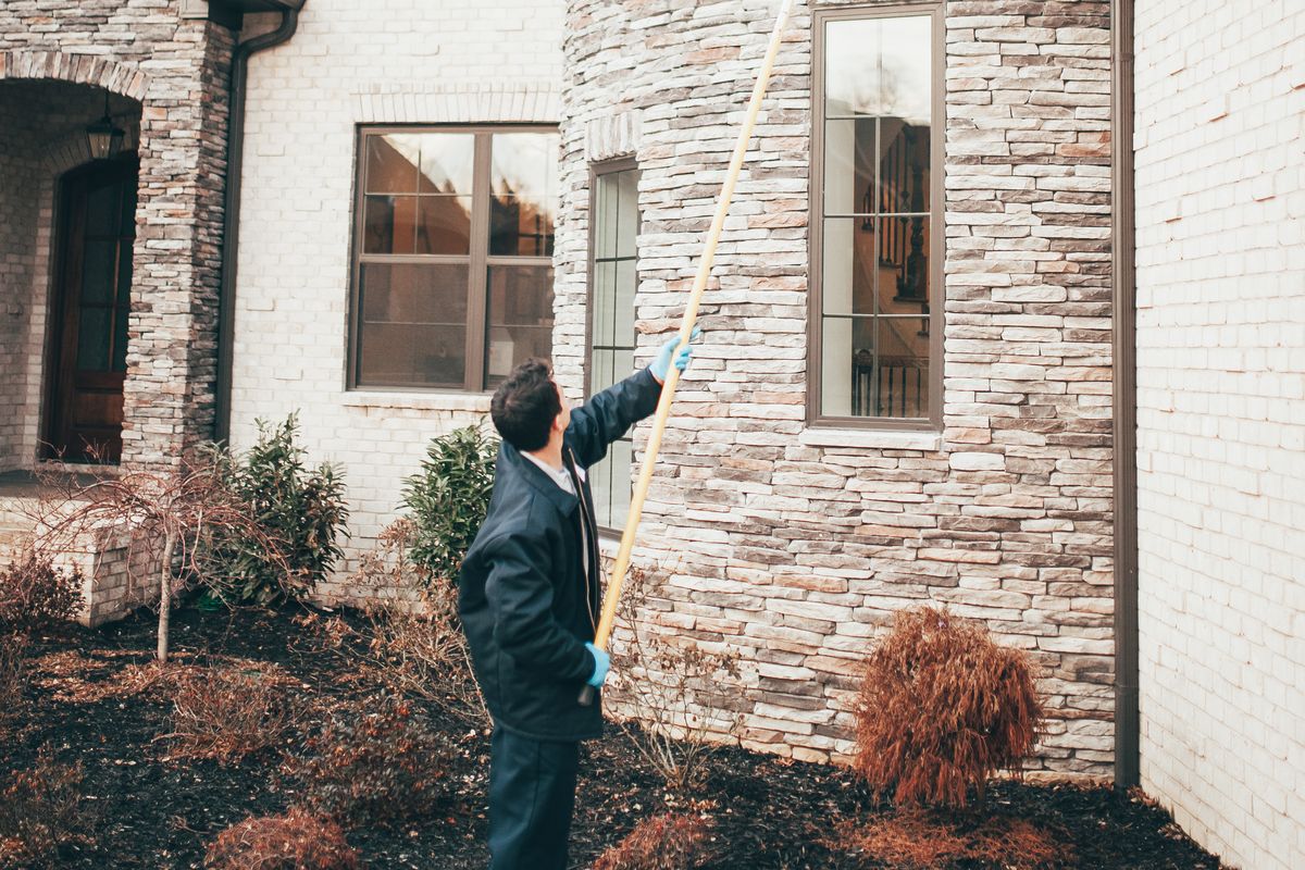 An Urbanex technician reaching a home's second-story windows and eaves with an extension pole