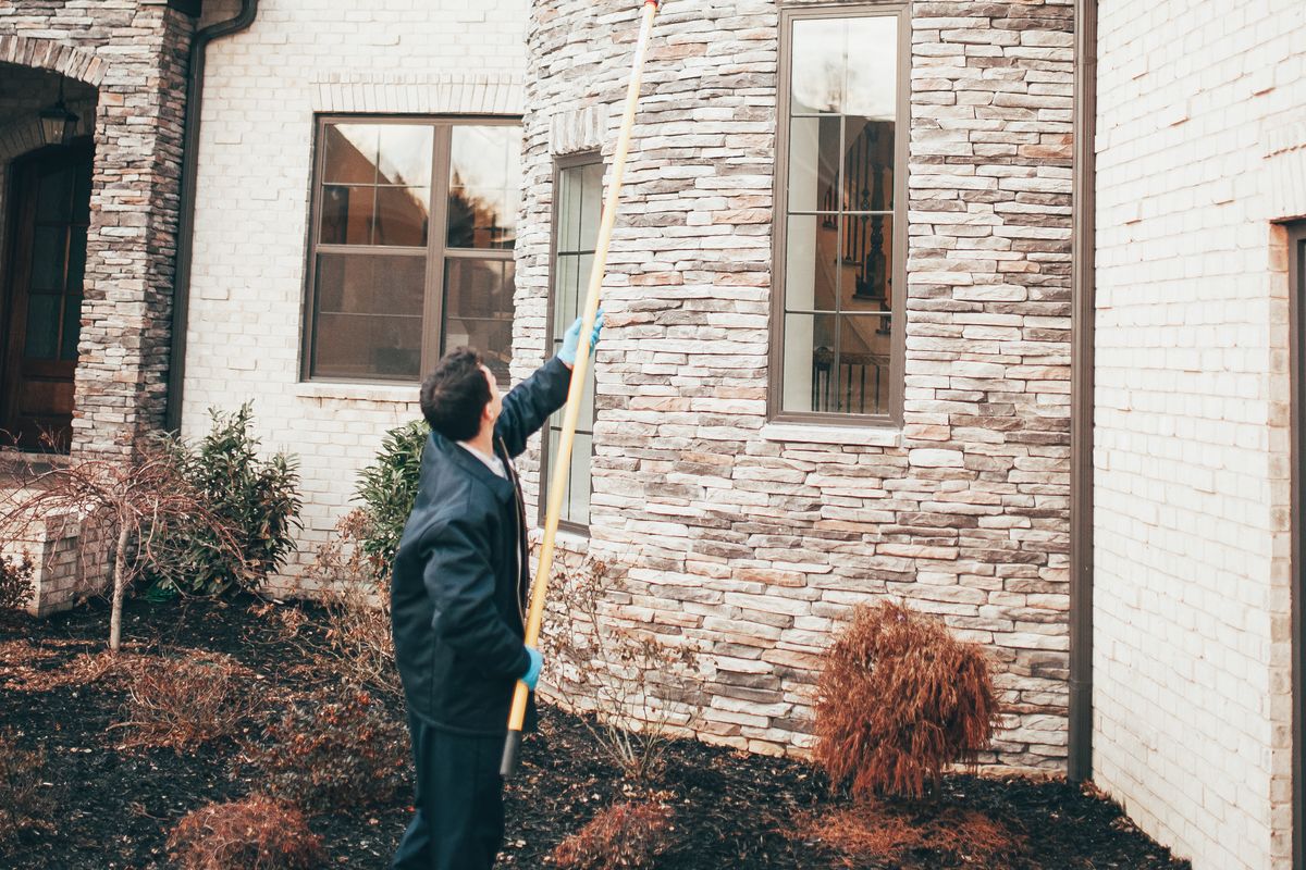 An Urbanex technician treating a home's stone turret and window lines with an extension pole