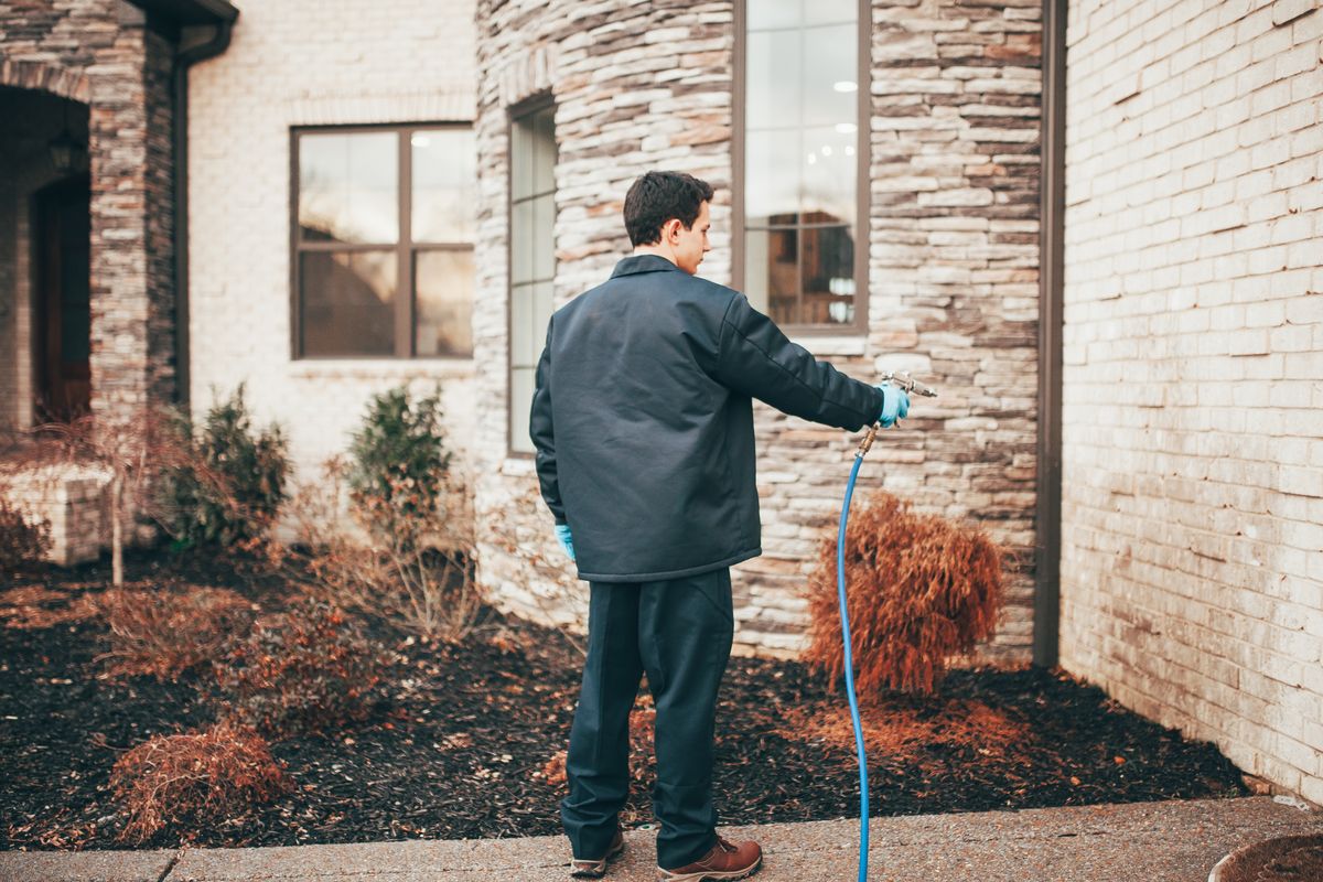 An Urbanex technician treating the foundation line and beds along a home's exterior wall