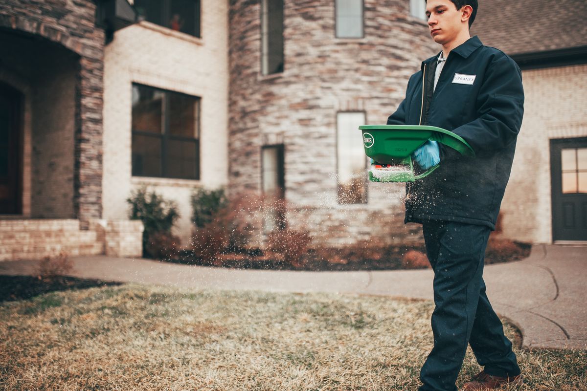 An Urbanex technician spreading granular treatment across a front lawn