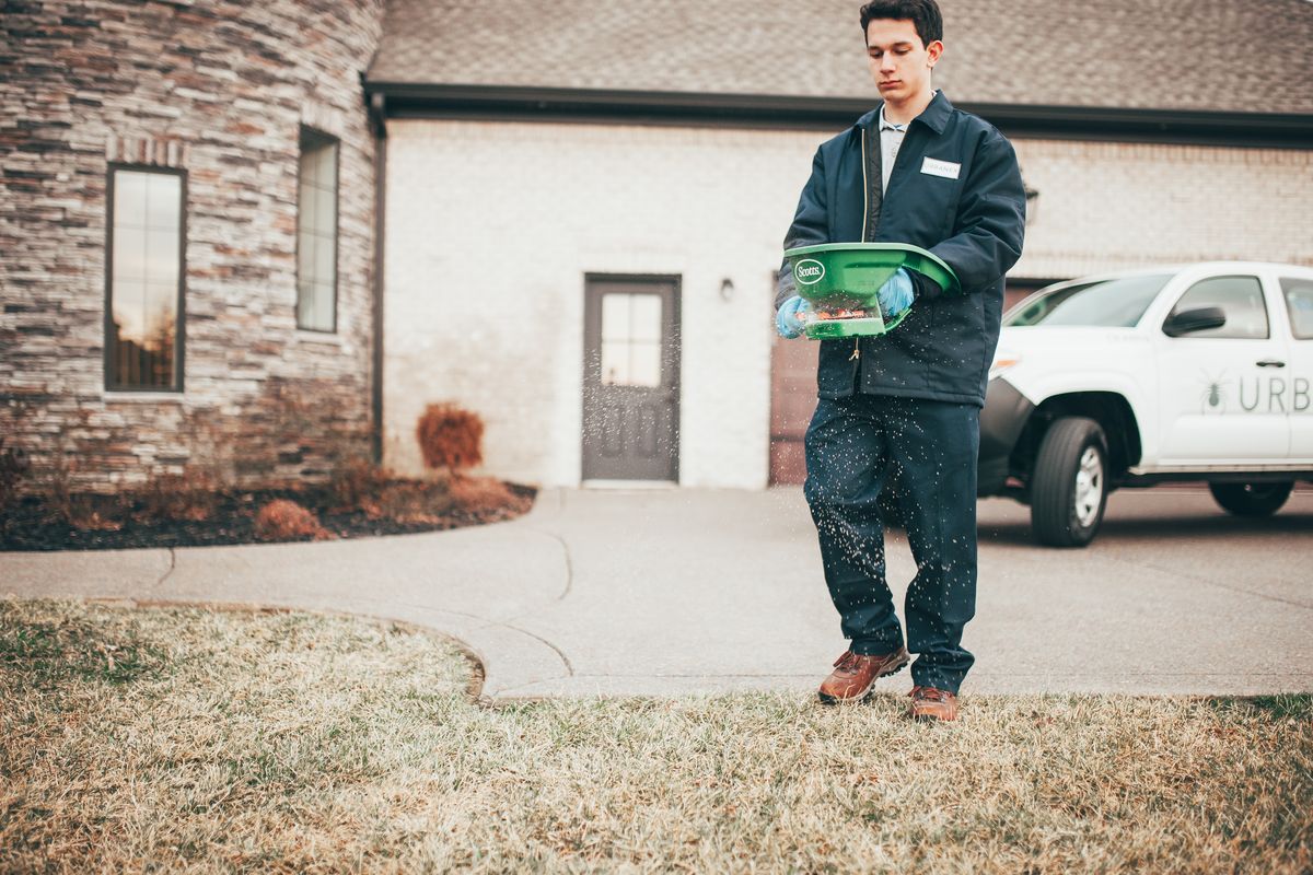 An Urbanex technician applying granular treatment to a front lawn beside an Urbanex truck