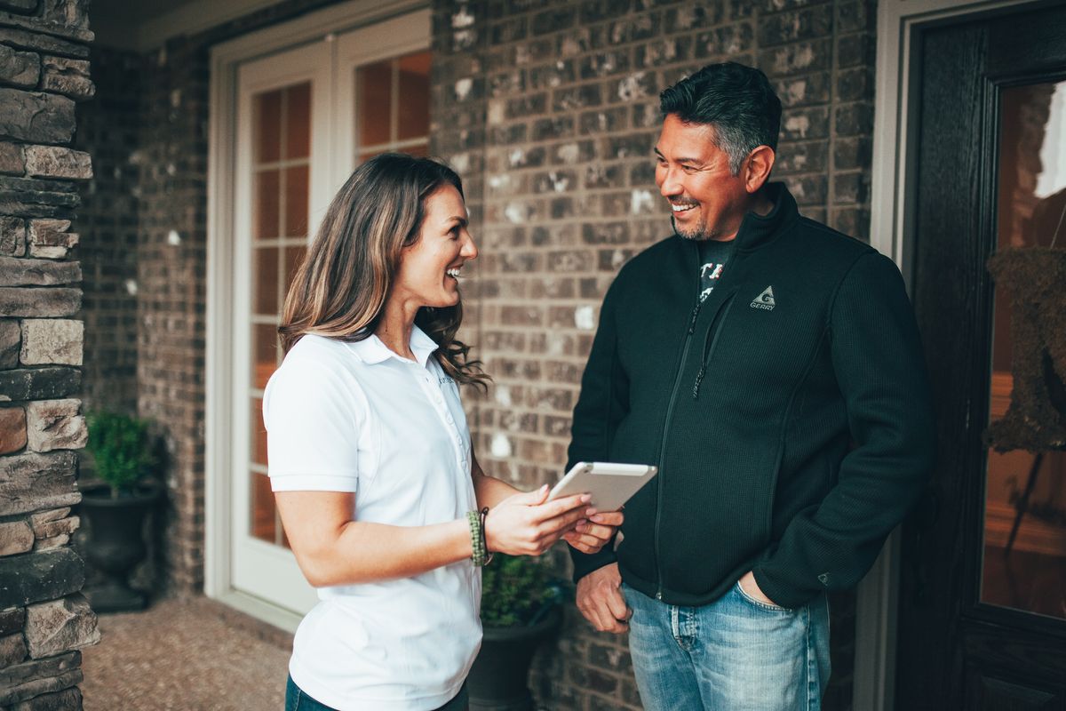 An Urbanex technician reviewing service findings on a tablet with a smiling homeowner at his front door