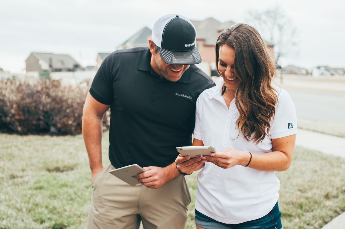An Urbanex technician and a homeowner smiling as they look over tablets together outside her home