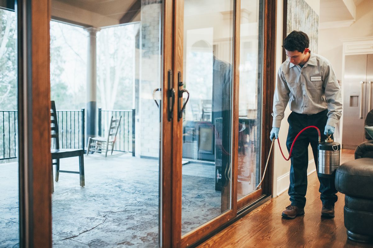 An Urbanex technician spraying along the interior sliding-door track of a home