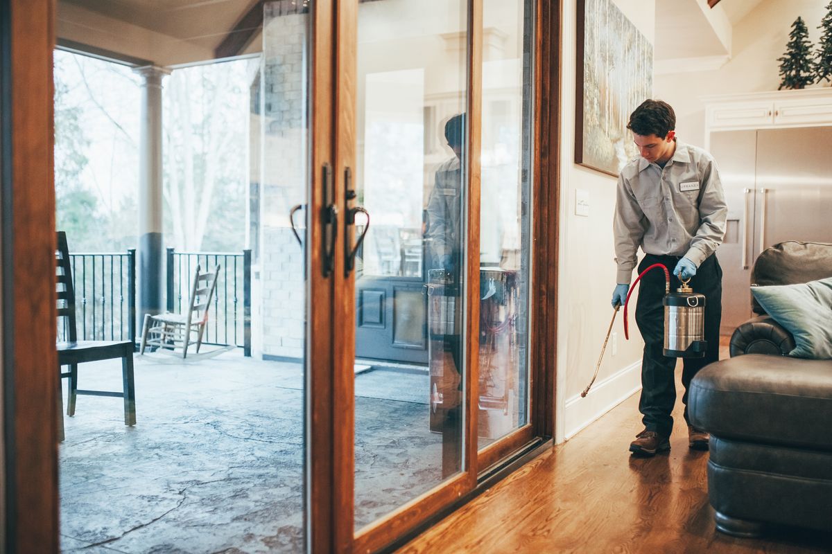 An Urbanex technician treating interior baseboards beside a home's sliding glass doors