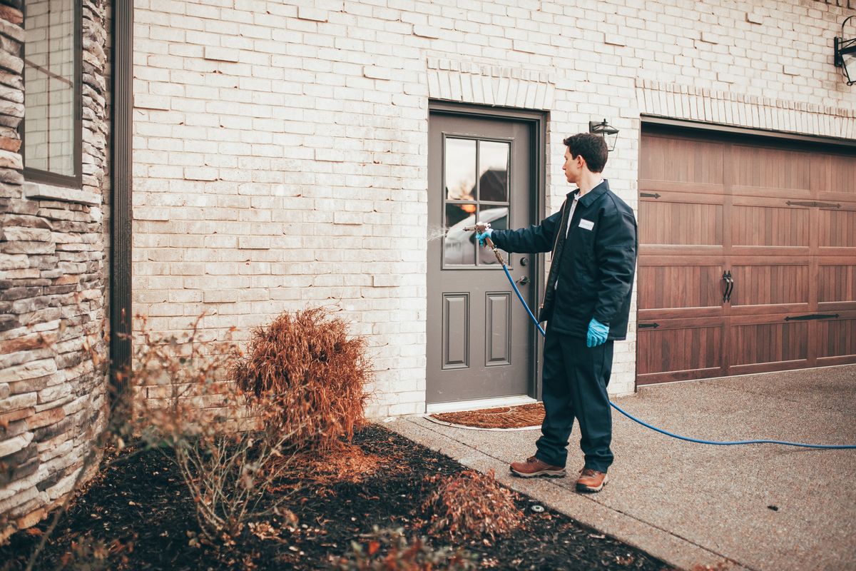 An Urbanex technician spraying the foundation beds beside a home's garage entry door