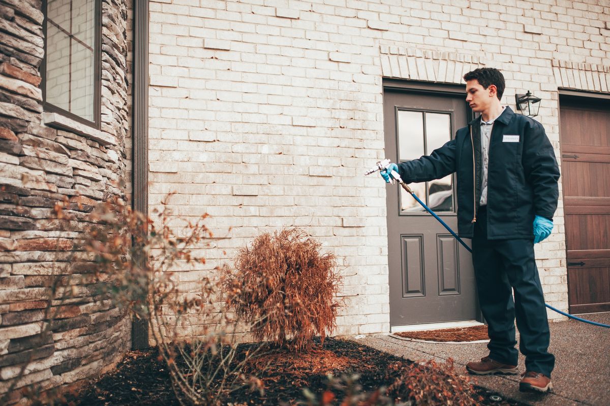 An Urbanex technician treating the perimeter of a home's exterior near the entry door